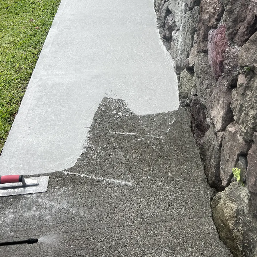Grey concrete coating being applied to outdoor path next to rock wall